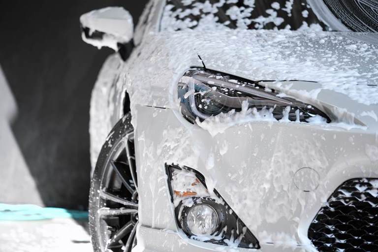 Front view of white sports car covered with water, washing foam, and soap on hood & bumper